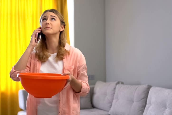Woman holding orange bowl after noticing roof leaking.
