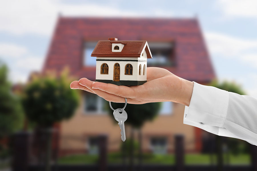 A hand holds a small model house with a single metal key hanging from the base, a symbolic image for those seeking home buying tips.